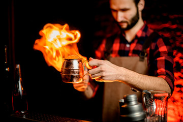 bartender holds metal cup with cocktail and sets it on fire.