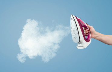 Female hand holds the iron with steam on a blue background