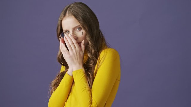 A pretty nice teenage girl is afraid of something standing isolated over a purple background in studio