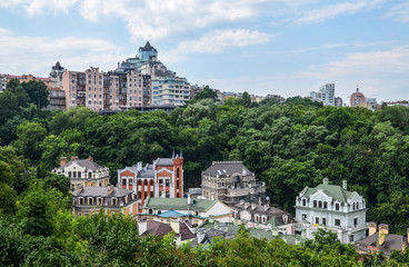 Fototapeta na wymiar Cute and colorful beautiful houses surrounded by trees at Vozdvizhenka and modern residential buildings on background. Summer Time in historical part of Kyiv - Podol 