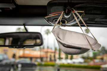 Face mask clipped with sunglasses on visor of interior of a car in a shooping center parking lot during the Coronavirus pandemic
