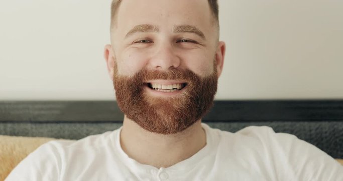 Close up view of cheerful bearded man having good mood and looking to camera. Portrait of handsome guy in 30s turning head and smiling while posing. Concept of people and emotions.