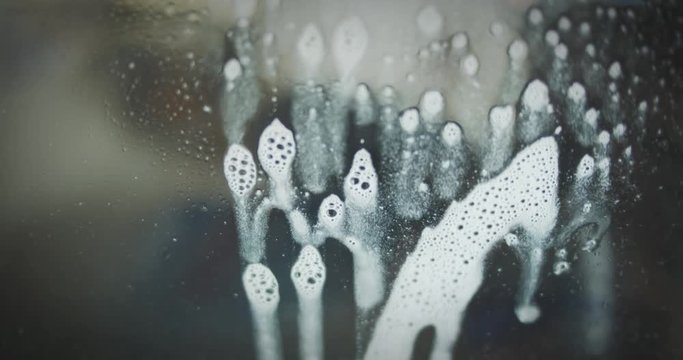 Cleaning spray is sprayed from behind onto a glass pane and then slowly runs down the glass. Close-Up.
