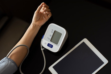 Woman takeing blood pressure by using digital sphygmomanometer with digital tablet computer on the desk. Medical and healthcare concept.