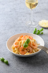 Italian pasta spaghetti with shrimps and glass of white wine on gray table. Close up.