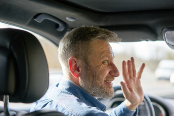 Profile of a friendly car driver with graying hair and beard greeting someone with his hand