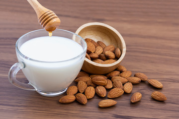 Closeup glass cup of almond milk with almonds seeds in wooden bowl with honey isolated on wood table background.