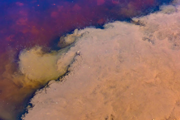 Fototapeta na wymiar Caustic toxic emissions brown, purple into the pond, bright contrasting spots on the water. The spread of poison in the ecosystem. The concept of pollution of life threatening, ecology.