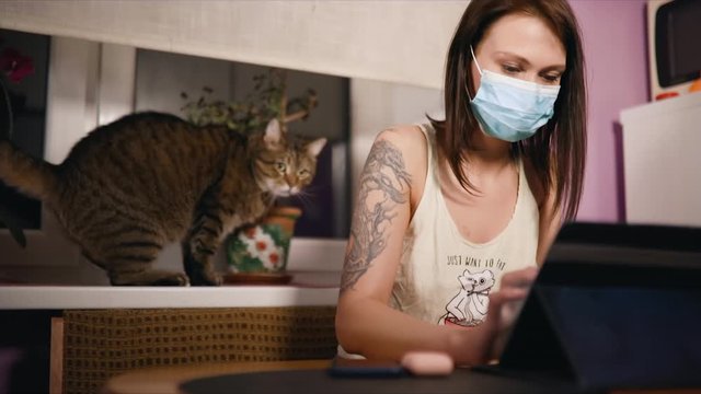 Brunette woman in surgical face mask with cat works from home