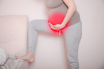 Pregnant woman with a strong pain massaging her backache. Pregnant tired exhausted woman with stomach and leg issues at home on a couch, being sick.