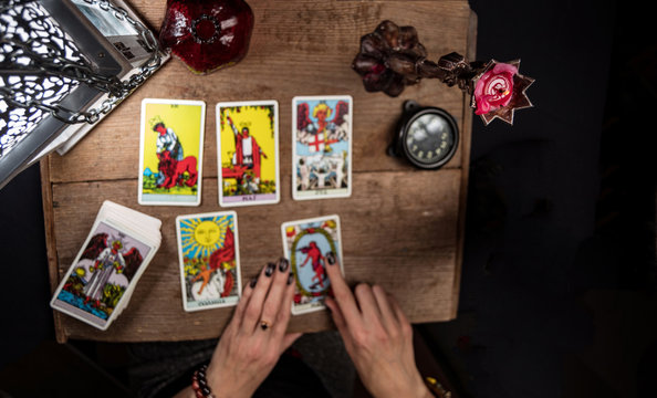 The fortune teller lays out on a wooden table the tarot cards by the light of a lantern and a candle. Selective focus..