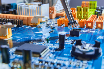 Electrician man fixing microelectronic board holding the microchip in tweezers and repairing electronic motherboard.