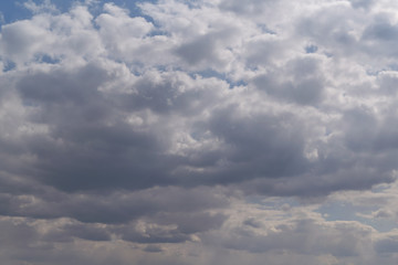 Obraz premium Many Cumulus and rain clouds of various shapes, sizes, and colors covered the blue sky. On the right side, the sun's rays break through from above. In the distance, the rain begins to fall.