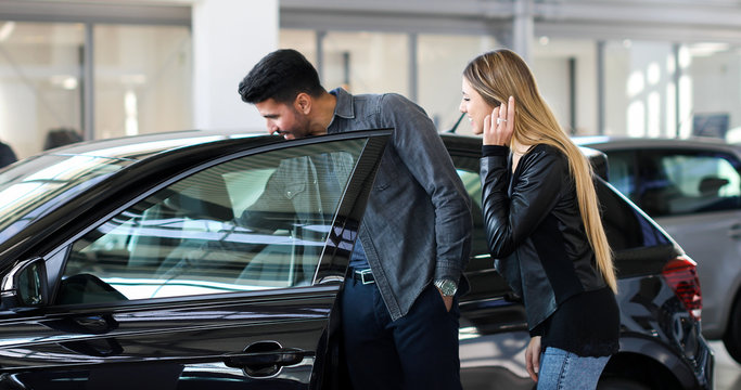 Young Couple Choosing New Car For Buying In Dealership Shop