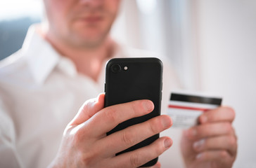 Close-up of a businessman using a smartphone for paying cashless, holding a credit card in the other hand