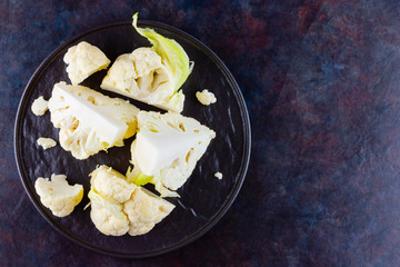 Cauliflower on a black plate. Sliced cauliflower on a dark background. Slices of organic cabbage on a plate. Top view. Copy space