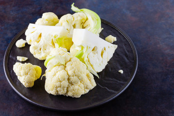 Cauliflower on a black plate. Sliced cauliflower on a dark background. Slices of organic cabbage on a plate. Top view. Copy space