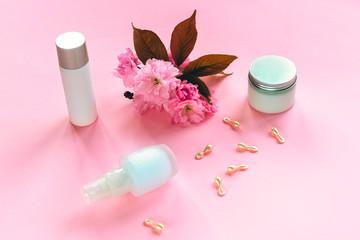 Obraz na płótnie Canvas Natural organic beauty skincare products. Serum, cream jar and beauty capsules unbranded blank packages. Cherry blossom decoration. Top view, flat lay, copy space.