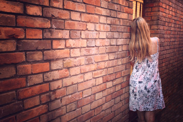 Back view of a woman leaning alone on brick wall