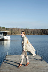 Happy young woman walks on a pier against the background of a boat and a lake. Women's holiday.