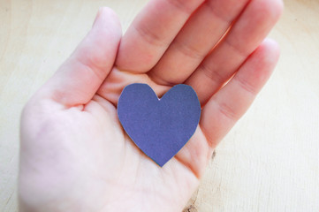 Fototapeta premium Hand holds a purple heart. Expression of understanding and compassionate love. Love and caring. The concept of parents and children. Military medal for wounded soldiers.