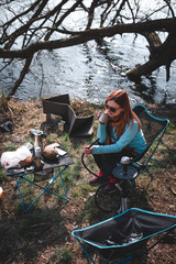 Girl smokes a hookah on the nature. Camping outdoor recreation. Lake. Portable, folding equipment for hiking trips. Lightweight, compact Chair and table made of aluminum tubes. Vertical photo
