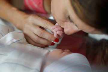 A mother holds her newborn infants hand in the hospital bassinet 