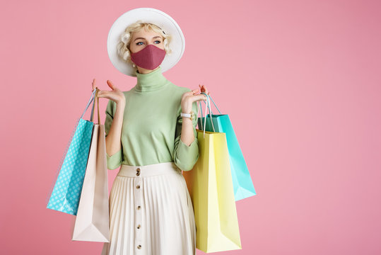 Spring shopping during quarantine conception: fashionable woman wearing protective mask posing with colorful paper bags. Pink background. Copy, empty space for text