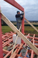 Joiner on roof installation, hammer hammering nail into wooden beam.
