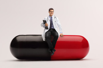 Young male doctor sitting on a big pill