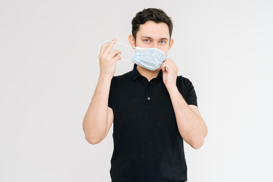 Portrait shot of young man in medical mask wearing casual black shirt, looking at camera, isolated on white background. Prevention of virus infection. Concept of Coronavirus COVID-19 Pandemic.