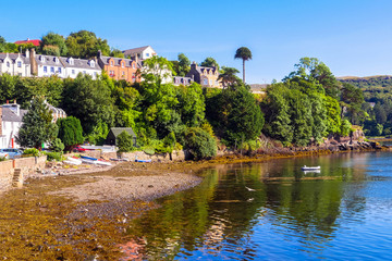 Portree, Isle of Skye, Scotland / United Kingdom - August 26, 2014: Beautiful houses over a pebble stone beach in the old town / Small recreation boats on the shore