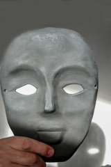 Black clay mask in a man's hand. Mask on a white background in a sunny morning in Ukraine. A clear shadow from the mask.