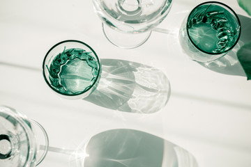 Glasses of water on white table. Harsh light through glasses, shadows. Clean minimalist contemporary art. Conceptual image. Green and white clean colors. Pure water in glass. Simple visual concept.
