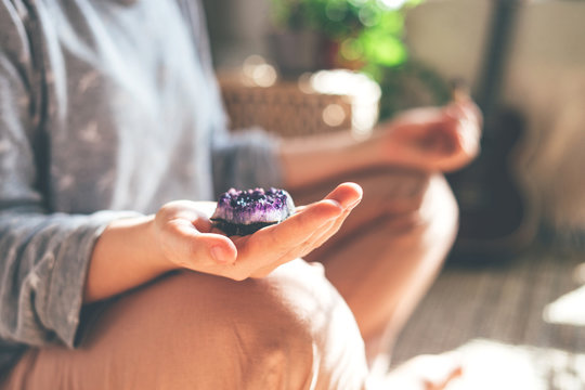 Young beautiful woman is meditating with a crystal quartz in her hand. Sits on the floor at home.