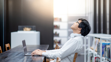 Asian man entrepreneur wearing glasses and headphones using laptop at home office. Businessman working with personal computer thinking about business project. Work smart with modern technology.