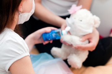 Little caucasian girl in medical face mask or surgical mask holding antiseptic bottle of hand sanitizer and disinfects toy, teddy bear. Coronavirus quarantine, protection from virus, hygiene concept.