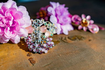 A composition of women's jewelry and accessories in pink on an old wooden surface. Brooch with colored stones, hairpins and flowers in delicate shades