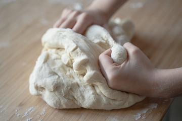 Fototapeta na wymiar little Caucasian girl hands working the dough on a wood cutting board