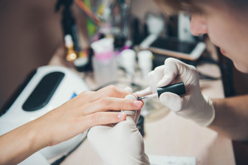 Master of manicure in rubber gloves makes a manicure  on the nails of a woman. Closeup of beautiful female hands applying transparent nail polish on healthy natural woman's nails in beauty salon.