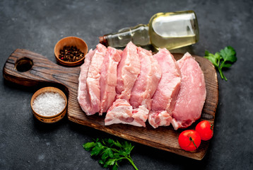 raw pork steaks with spices on a cutting board on a stone background
