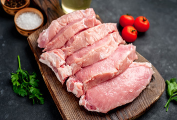 raw pork steaks with spices on a cutting board on a stone background