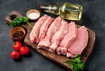 raw pork steaks with spices on a cutting board on a stone background