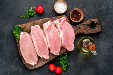 raw pork steaks with spices on a cutting board on a stone background