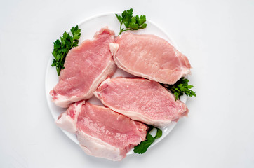 raw pork steaks with spices on a white plate on a white background