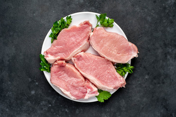 raw pork steaks with spices on a white plate on a concrete background