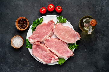 raw pork steaks with spices on a white plate on a concrete background