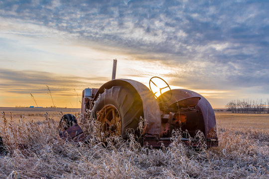 Sunburst at sunset over a vintage tractor abandoned in tall grass on the prairies in Saskatchewan
