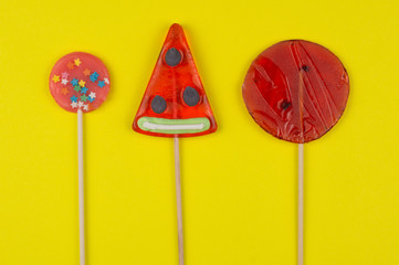 Three delicious candy caramel lollipops bright red on a yellow background flat lay