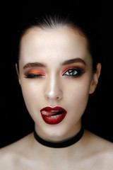 Close-up portrait of gorgeous young woman with red lips and bright makeup of eyes looks to the camera.. Beautiful girl with a healthy clean skin against black background.